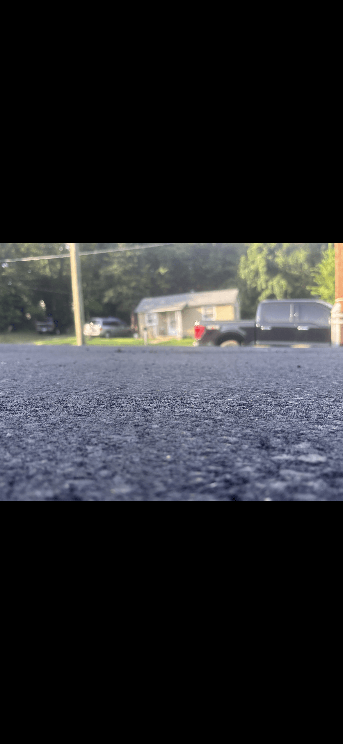Low-angle view of textured asphalt pavement with a blurry house and black truck in background.