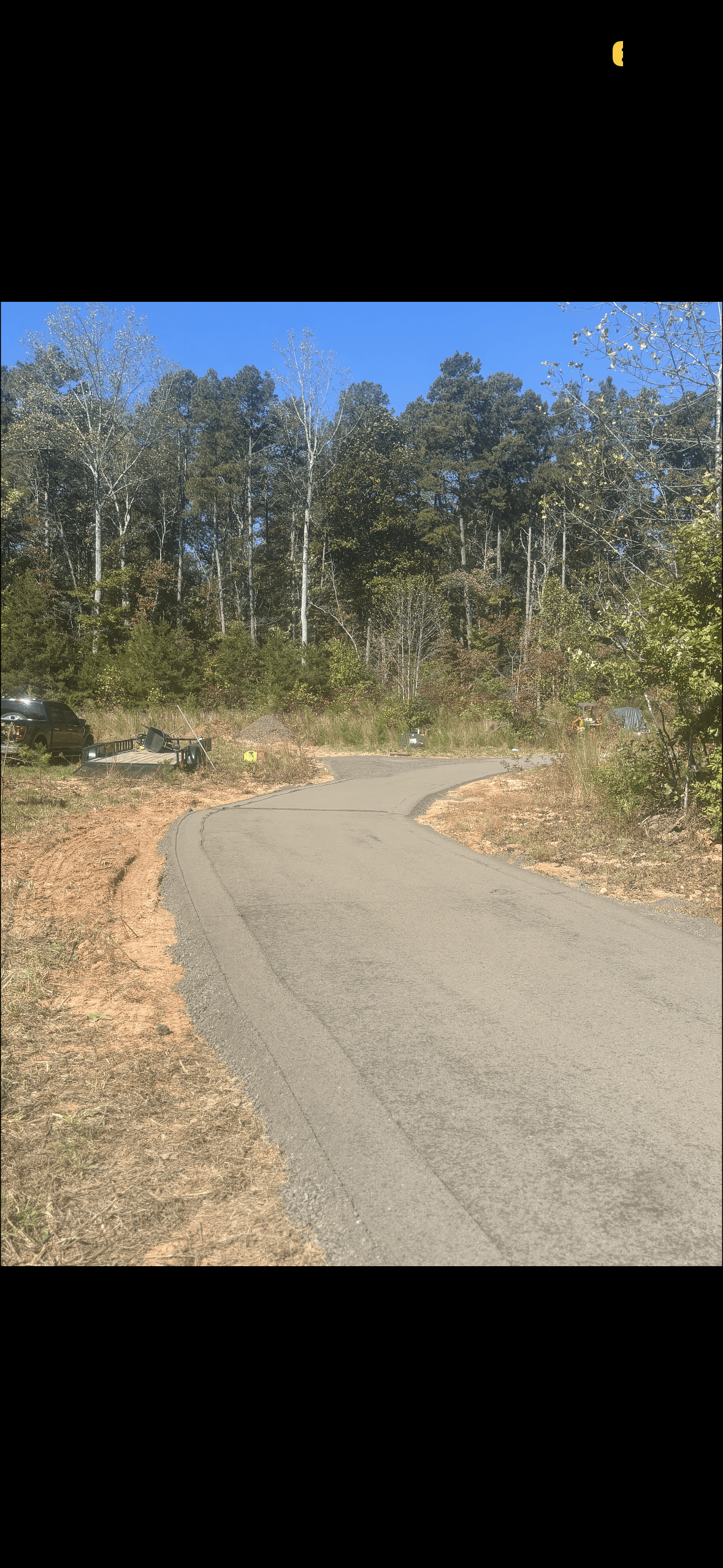 Curved gray gravel driveway leading toward a dense forest under a clear blue sky.