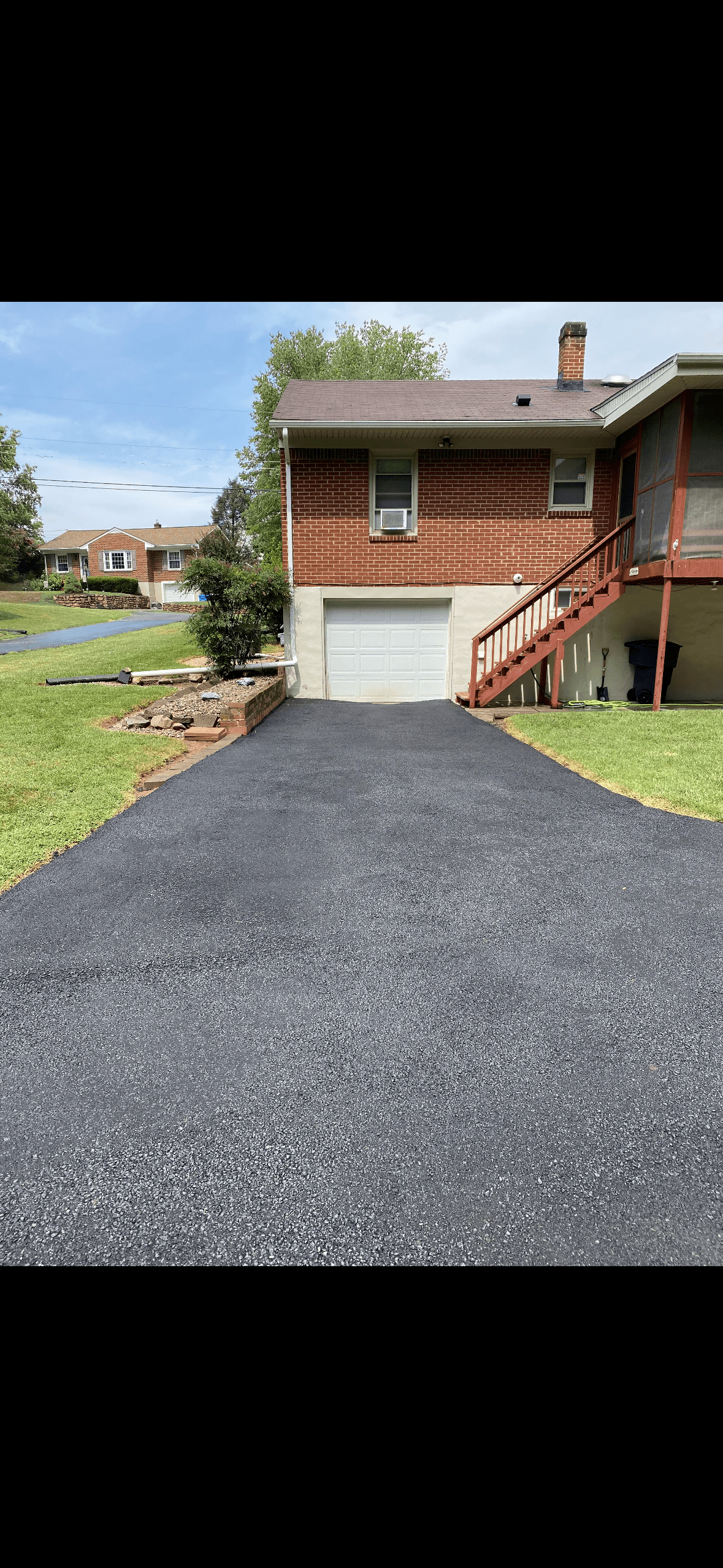 Freshly sealed black asphalt driveway leading to a white garage door on a brick house.